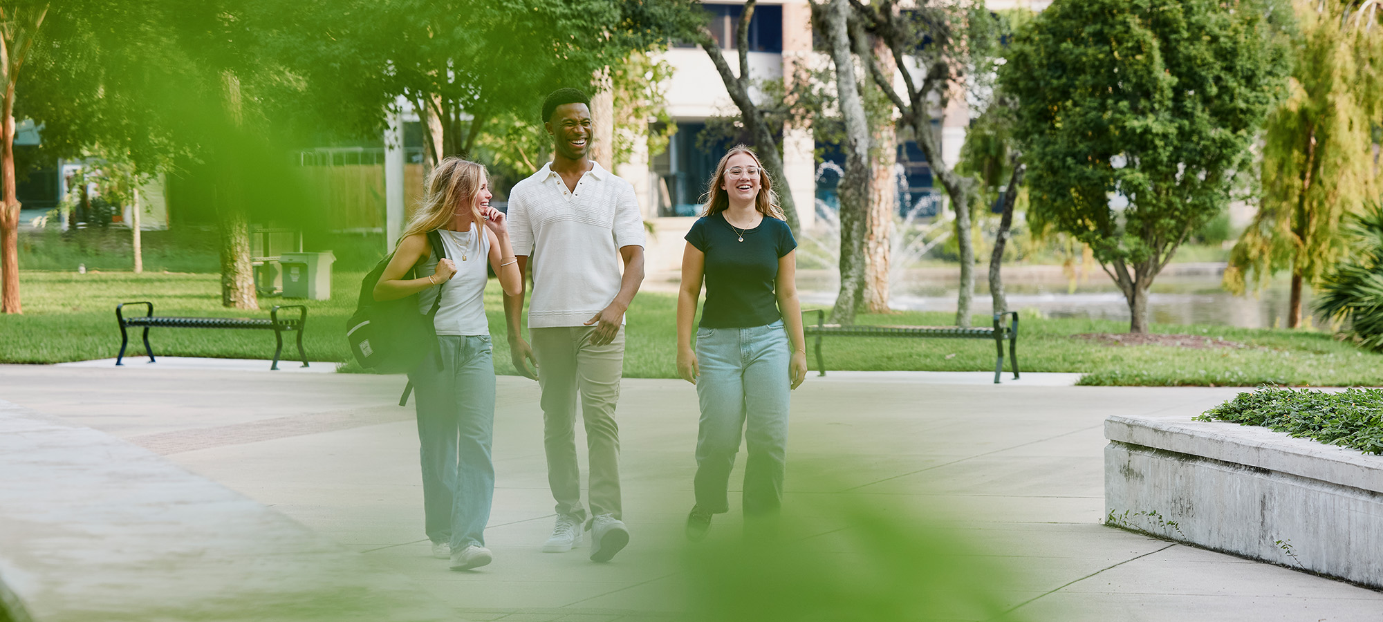 Three students walking through campus together while smiling and laughing